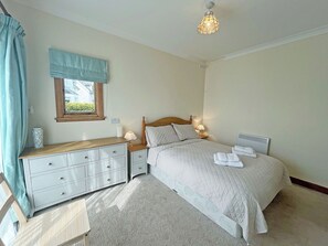 Une chambre à coucher comprenant un lit, des tables de chevet, une commode, une fenêtre avec des rideaux et un luminaire au plafond.