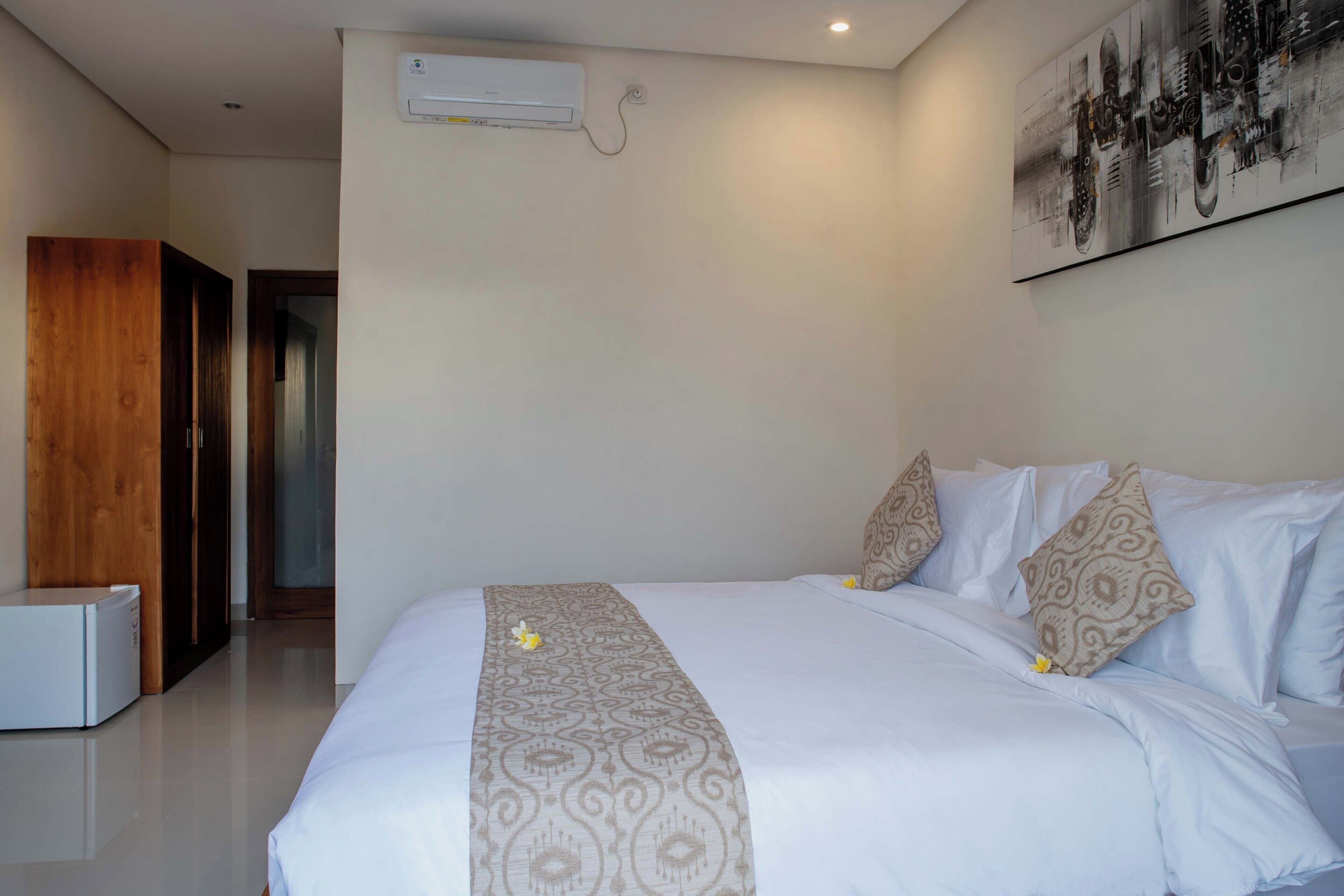 Een hotelkamer met een bed, een wandairconditioner en een deur naar een andere kamer.