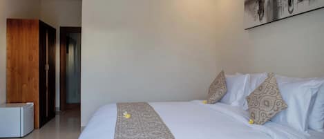 Een hotelkamer met een bed, een wandairconditioner en een deur naar een andere kamer.