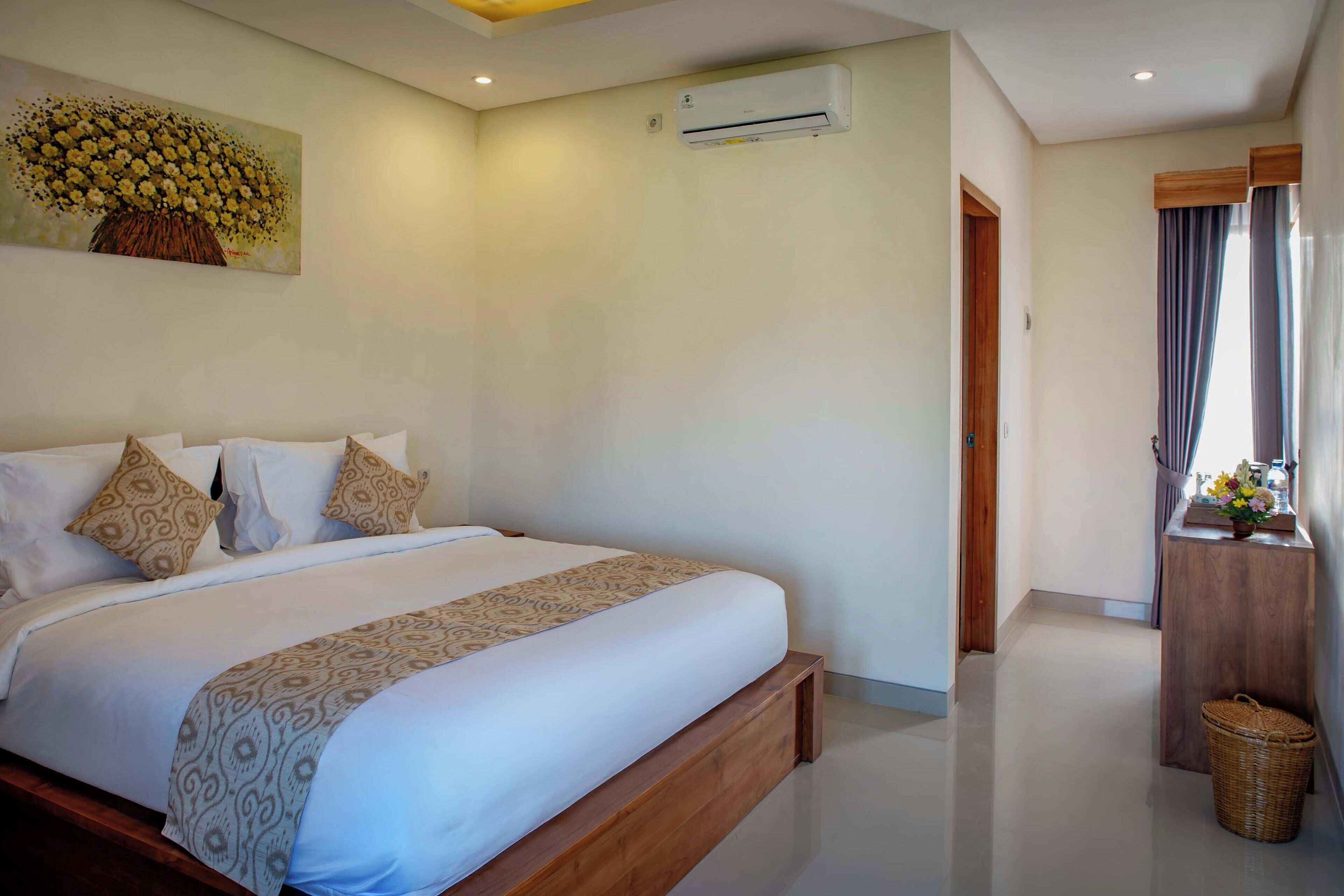 A bedroom with a large bed, a wooden headboard, a wall-mounted air conditioner, and a small wooden table with a basket.