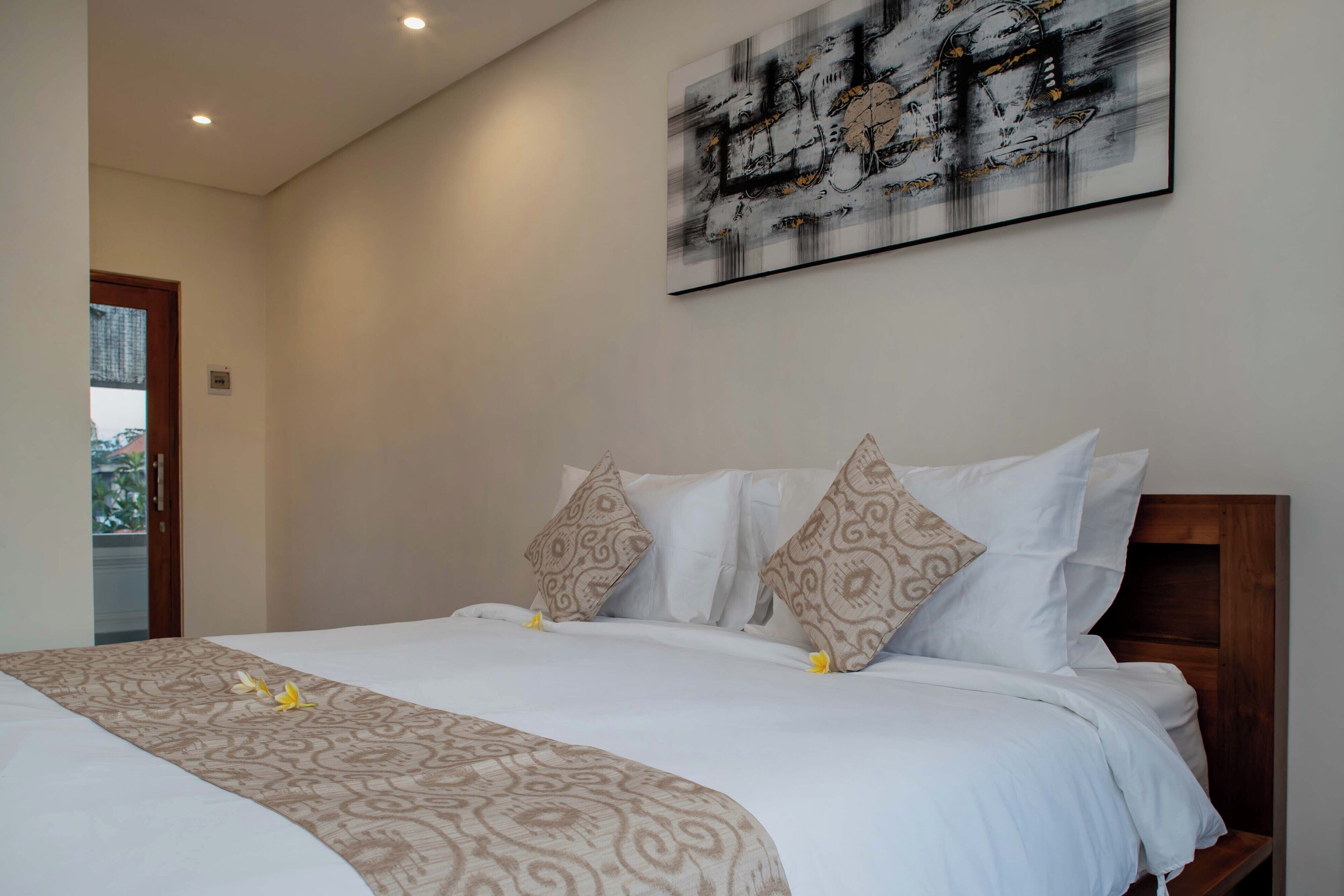 Een netjes opgemaakt bed met een bedsprei en kussens met een patroon, een houten hoofdbord en een groot abstract schilderij aan de muur.