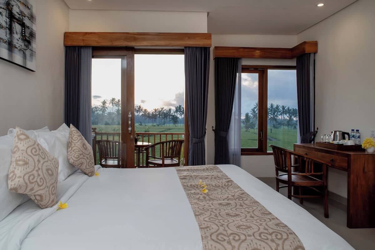 Una habitación de hotel con una cama grande, un escritorio y un balcón con vistas a palmeras.
