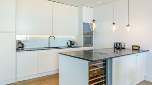 Una cocina moderna con armarios blancos, una isla central, horno empotrado e iluminación colgante.