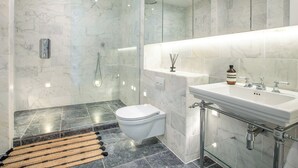 Un baño moderno con ducha envuelta en vidrio, inodoro blanco, piso de mármol y puerta de vidrio para la ducha.