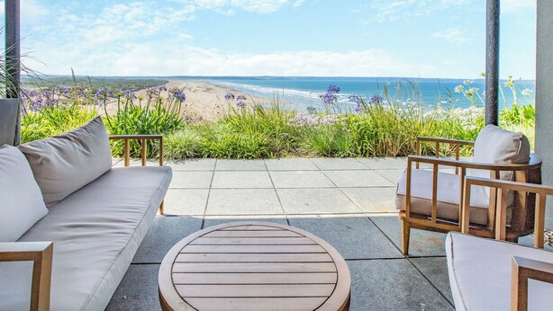 Un patio techado con vista a la playa, una mesa redonda de madera y un sofá.