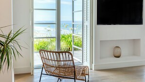 Una habitación con una televisión montada en la pared, una silla de mimbre y un ventanal corredero que da a un balcón con vistas al océano.