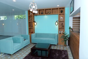 Una sala de estar moderna con un sofá azul claro, un separador de vidrio y un estante de madera con objetos decorativos.