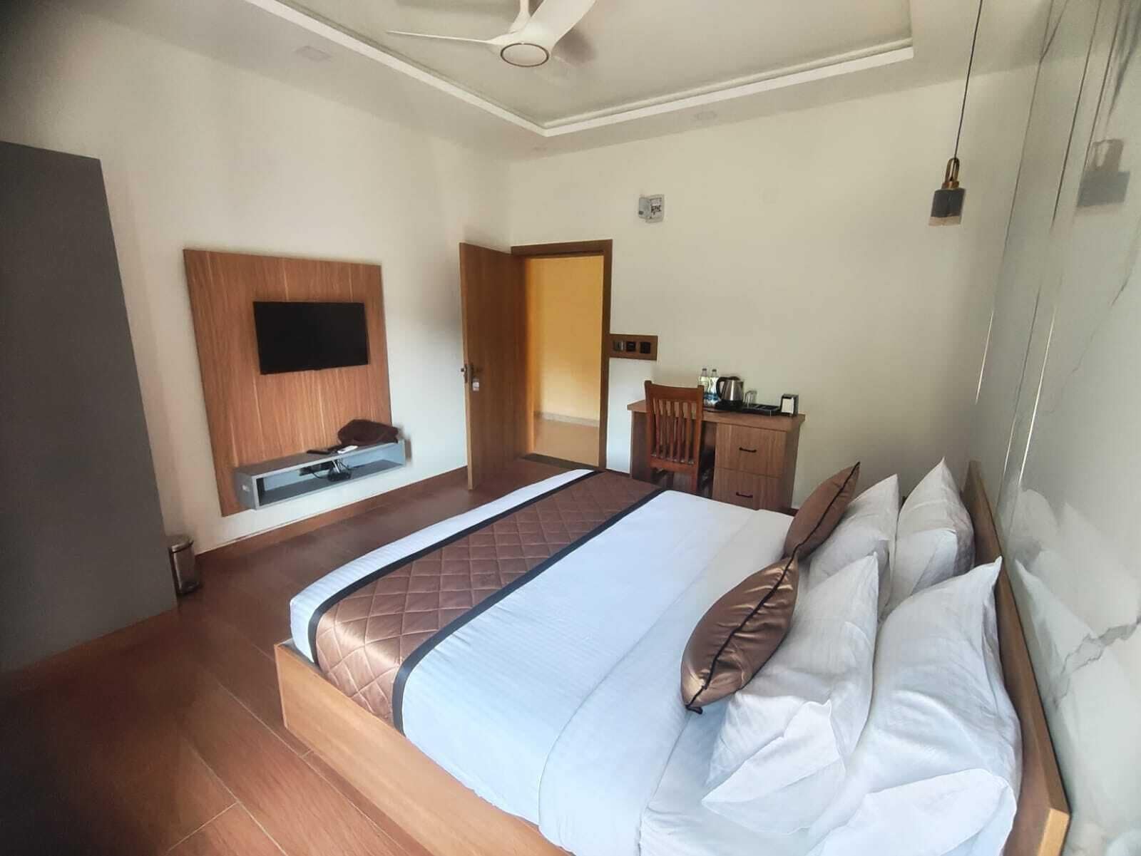 Hotelkamer met een bed, een bureau, een stoel, een aan de muur bevestigde televisie en een plafondventilator.