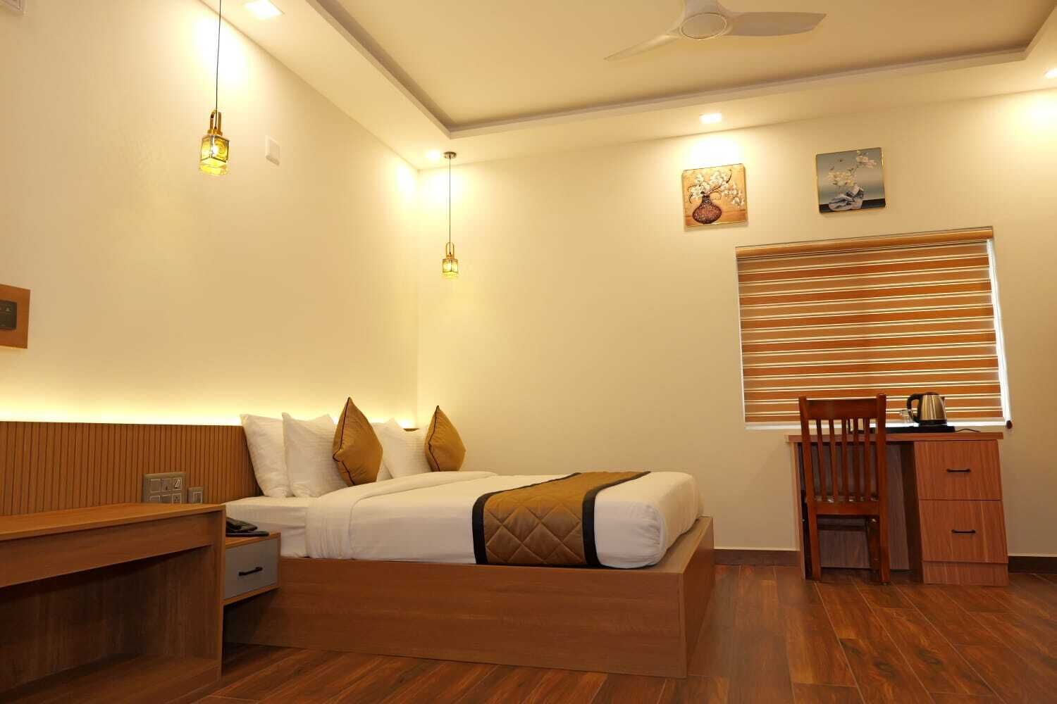 A bedroom with a bed, bedside table, lamp, and a desk with a chair.