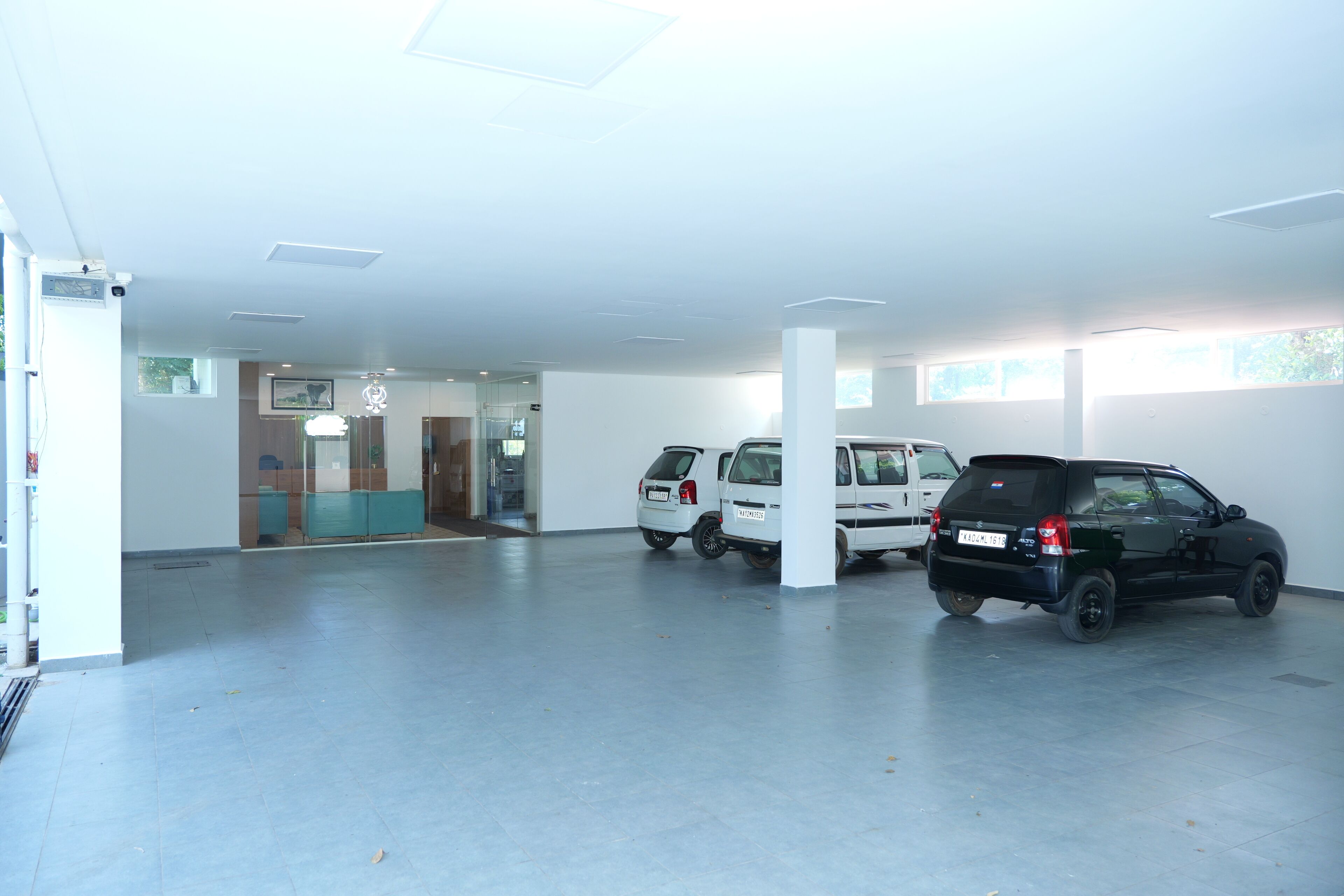 Un garaje con dos coches estacionados, un área de recepción con mostrador azul y una puerta de cristal que da a un espacio interior.