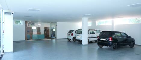 Un garaje con dos coches estacionados, un área de recepción con mostrador azul y una puerta de cristal que da a un espacio interior.