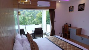 A hotel room with a bed, a desk, a chair, and a view of greenery outside.