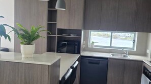 A modern kitchen with a dishwasher, a microwave, and a window providing a view of the outdoors. - Salt Apartments Unit 16, 12 Bright Place, Birtinya (Birtinya)
