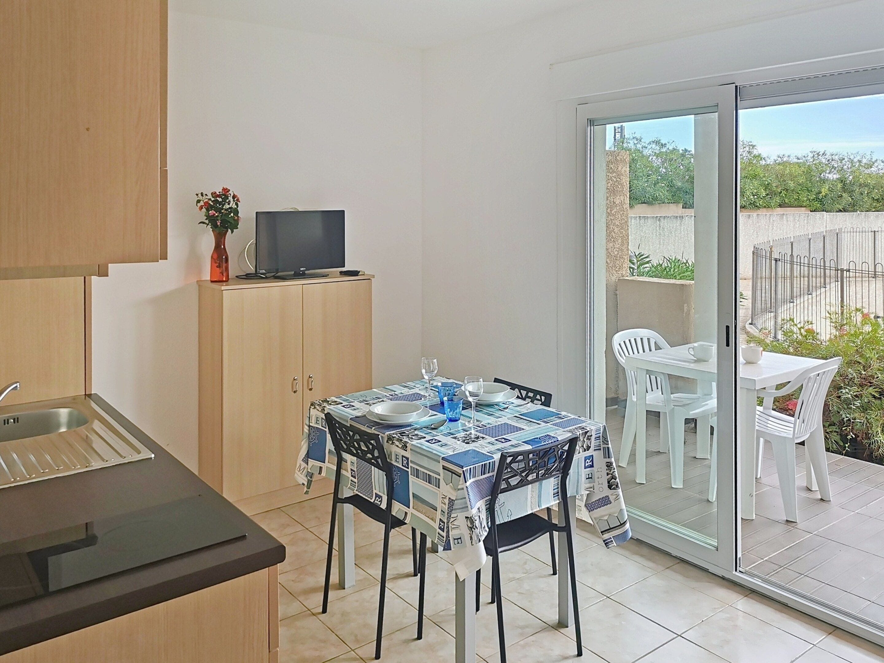 Cocina compacta con comedor, televisor en un mueble y vistas al exterior.