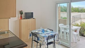 Cocina compacta con comedor, televisor en un mueble y vistas al exterior.