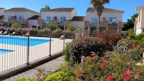 Um edifício residencial com piscina, cercado por uma grade e diversas plantas.