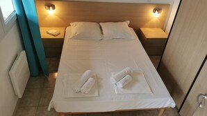 Uma cama bem arrumada com lençóis e toalhas brancas, duas luminárias laterais e uma janela com cortinas.