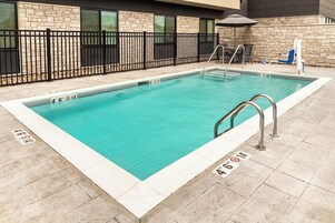 Una piscina rectangular con agua azul cristalina, rodeada por una cerca de metal negro y un muro de piedra.
