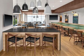 A modern restaurant with a central bar area, multiple seating options including booths and tables, pendant lighting, and artwork on the walls. - Fairfield by Marriott Inn & Suites Norwalk (Norwalk)