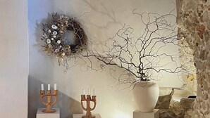 A room with a stone wall, a wooden ceiling, a white shelf with a candelabra, a vase, and a wreath. - Cozy and refined retreat in the heart of Fanjeaux (Fanjeaux)
