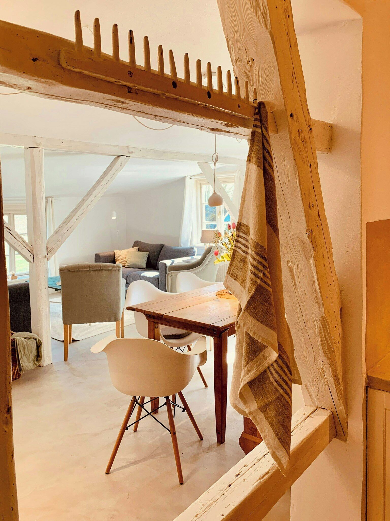 Ein Zimmer mit Holzbalken an der Decke, einem Esstisch mit Stühlen, einer Couch und einem Fenster mit Vorhängen.