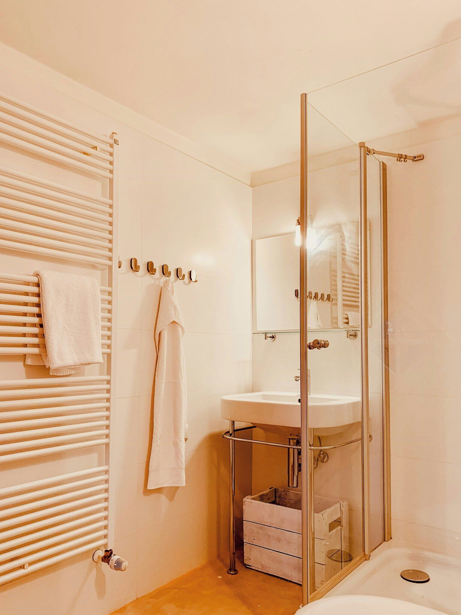 Un baño con cabina de ducha de vidrio, un lavamanos blanco y un perchero con toallas.