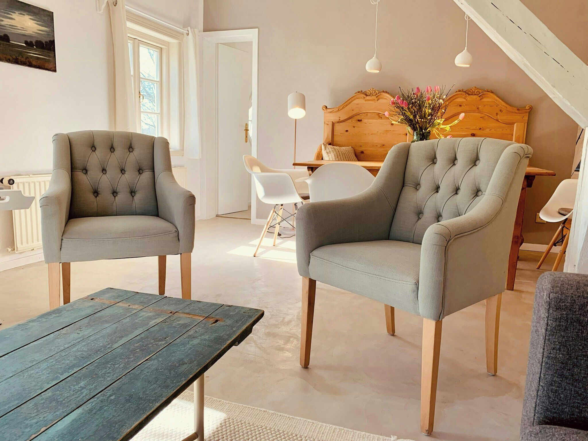 Una habitación con dos sillas tapizadas grises, una mesa de madera, un cabecero de madera y un techo blanco.