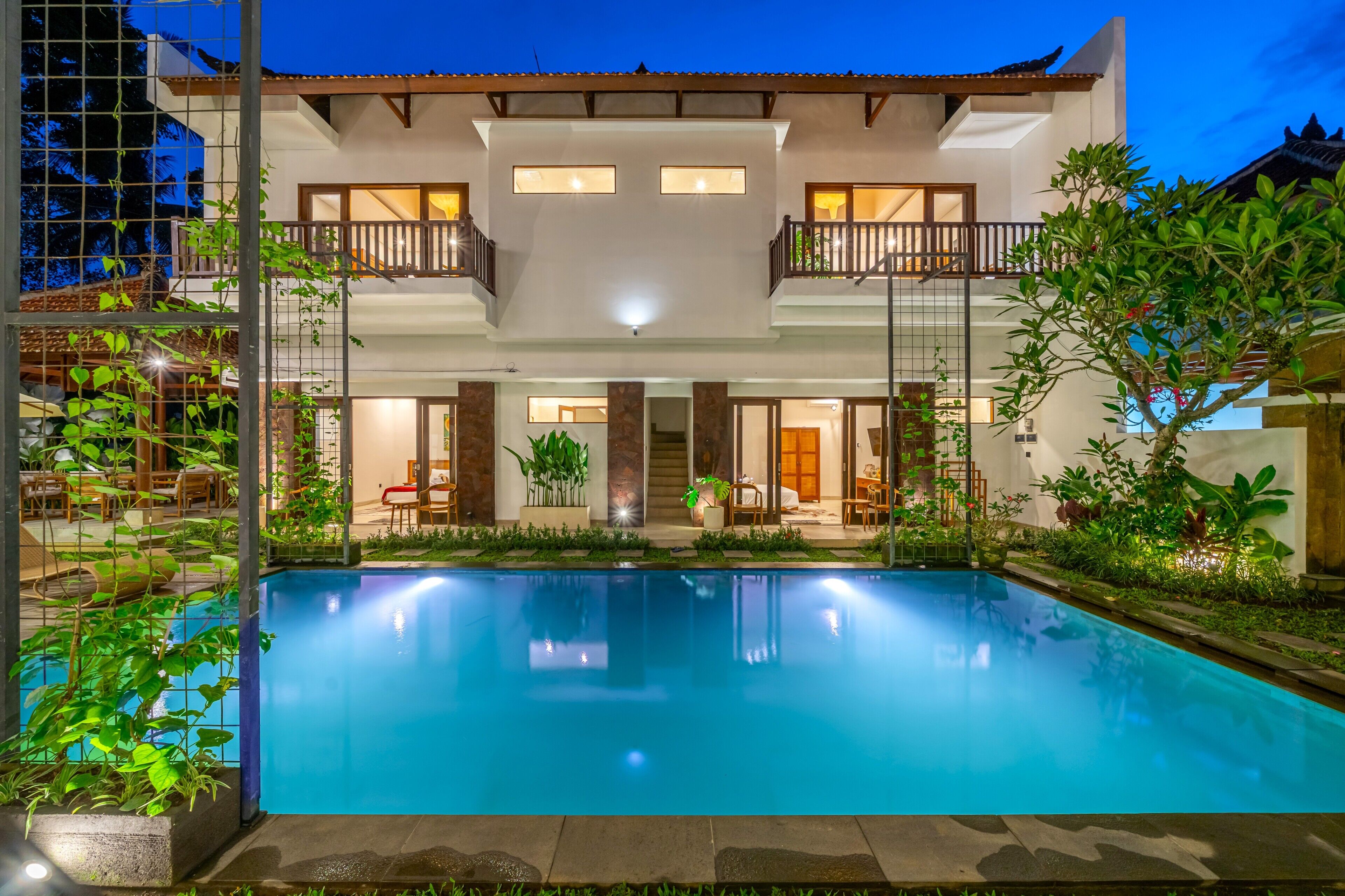 A two-story house with a swimming pool, outdoor seating, and a well-lit entrance.