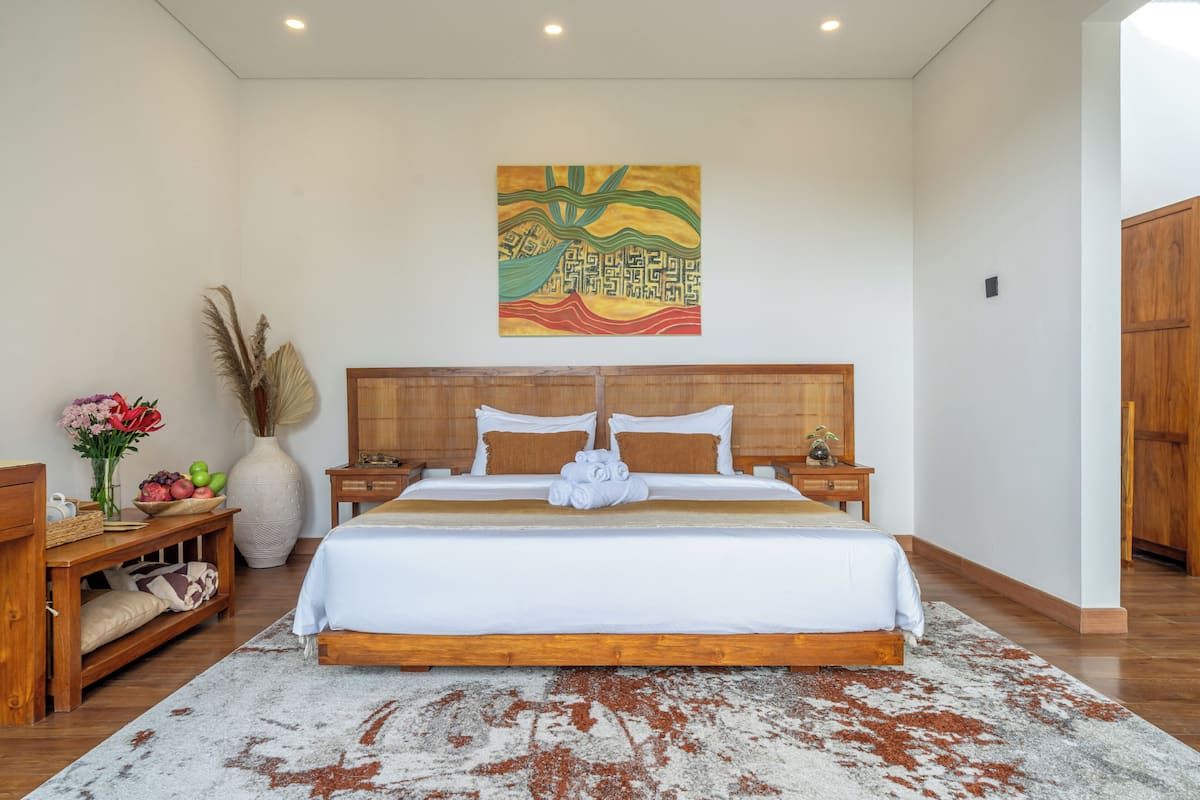 Ein großes Bett mit Holzrahmen, ein Nachttisch, eine Vase mit Blumen und ein Gemälde an der Wand.