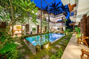 Una villa moderna con piscina, exuberante vegetación y un área exterior bien iluminada.