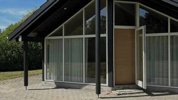 A modern building with a sloped roof, large glass windows, and a brick-paved entrance.