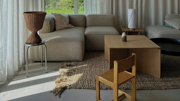 Una sala de estar moderna con techo de madera, un sofá modular, una mesa de centro, una silla y vistas a espacios verdes.