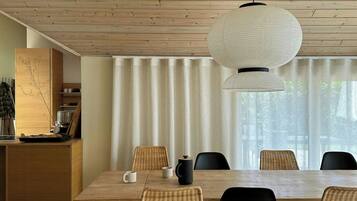 Un comedor moderno con techo de madera, una mesa grande, sillas de mimbre y una lámpara colgante.