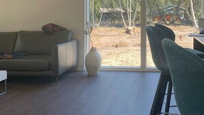 Une pièce spacieuse dotée d’une grande porte-fenêtre coulissante donnant sur un espace extérieur, ainsi que d’un canapé, d’un fauteuil et d’un vase posé sur le sol.