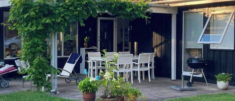 Eine Terrasse mit Tisch, Stühlen, einem Grill und Kübelpflanzen.