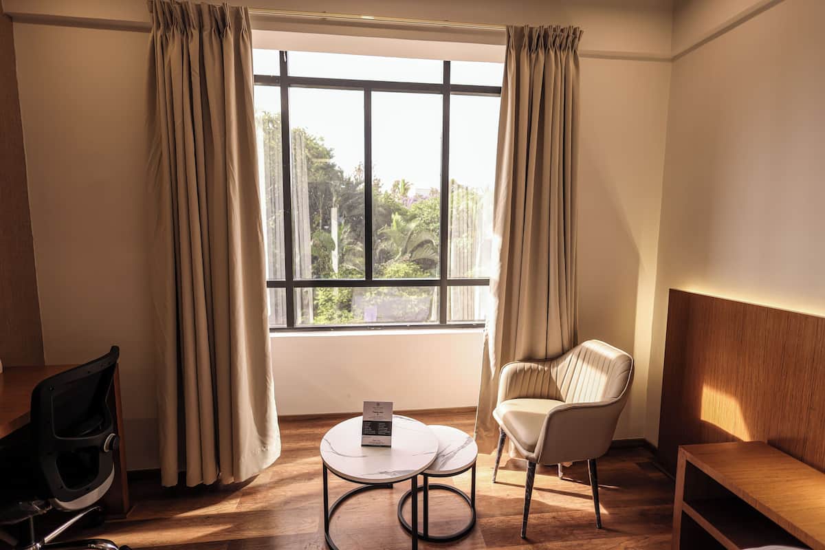 Um quarto com uma janela grande, uma cadeira, uma mesinha e um banco de madeira.