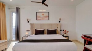 Un dormitorio con cama, ventilador de techo, mesita de noche, lámpara, un cuadro en la pared y vistas al exterior.