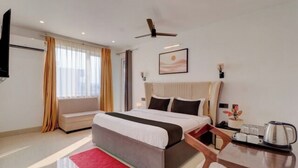 Habitación de hotel con cama, escritorio, silla, televisor, ventilador de techo y ventana con cortinas.