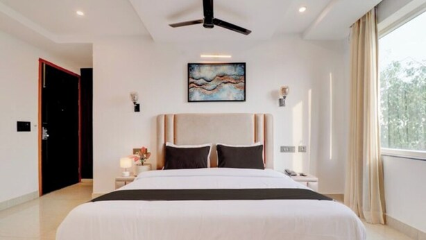 Un dormitorio moderno con una cama grande, un ventilador de techo, un cuadro en la pared y una ventana con cortinas.