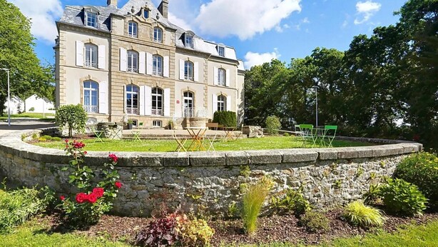 Ein großes, historisches Gebäude mit zahlreichen Fenstern und einer Steinmauer, die einen Garten umgibt.