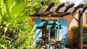 A patio with outdoor furniture, a pergola, and a building with blue shutters. - Family Maisonette in Provence (Les Mathes)