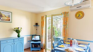 A room with a dining table set for two, a television on a stand, a vase with flowers, and a clock on the wall. - Family Maisonette in Provence (Les Mathes)