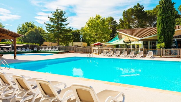 A swimming pool with lounge chairs, a covered area, and a building with a tiled roof. - Family Maisonette in Provence (Les Mathes)