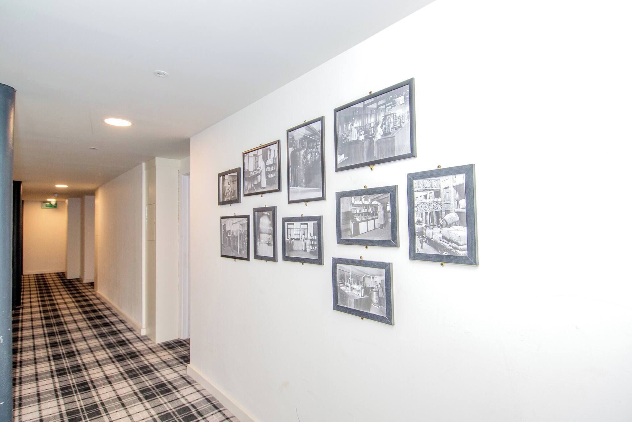 A hallway with a black and white checkered floor, white walls, and framed black and white photographs on the wall.