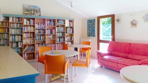 A room with a bookshelf, a pink sofa, and a dining area with orange chairs.