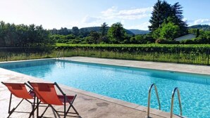 A swimming pool with a clear blue water, surrounded by a hedge and trees.