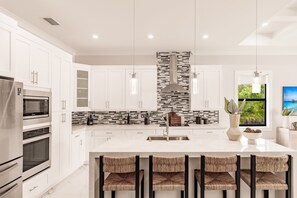 Una cocina moderna con armarios blancos, una isla central con taburetes y un lavadero de acero inoxidable, además de un salpicadero con diseño geométrico.