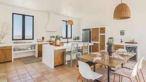 Una cucina moderna con mobili bianchi, un'area pranzo con tavolo e sedie in legno e ampie finestre.