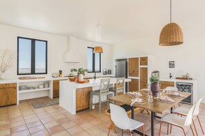 Eine moderne Küche mit weißen Schränken, ein Essbereich mit Holztisch und -stühlen sowie große Fenster.