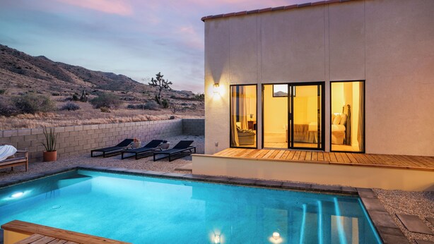 Una casa moderna con piscina, lettini da sole e un'area patio.